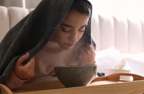 Girl sitting down in front of steaming bowl of water and a towel over her head